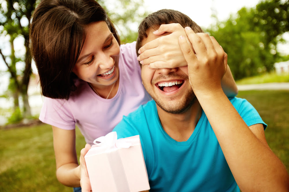 Frau ueberrascht ihren Freund mit einem Geschenk