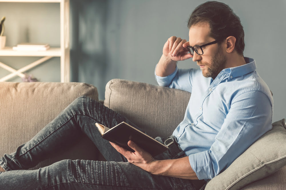 Mann liest Buch auf dem Sofa