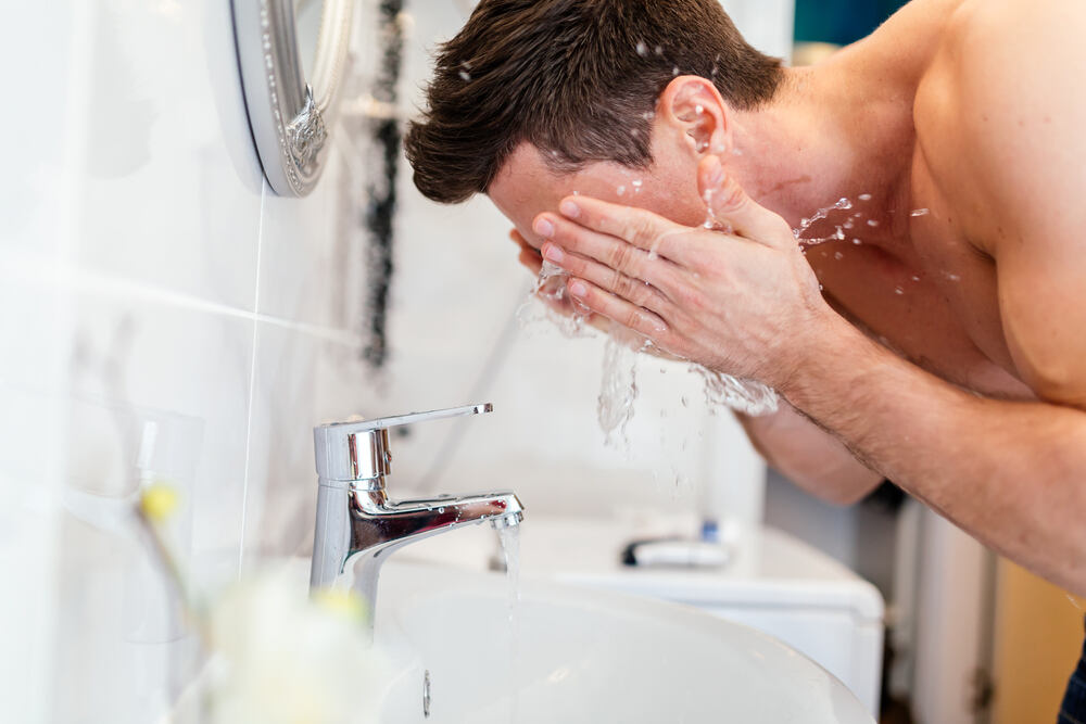 Mann wäscht sich sein Gesicht am Waschbecken